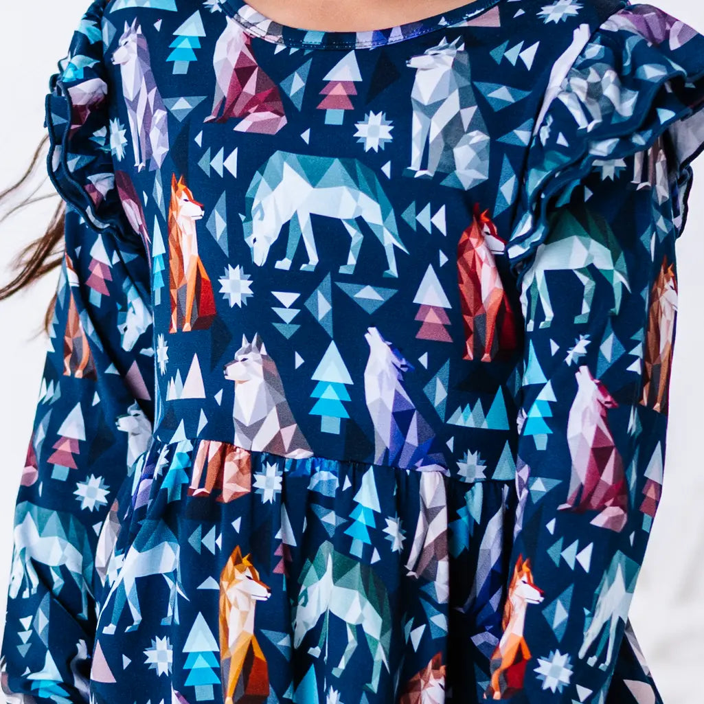 Close up of the front of a long sleeve twirl dress with flutter ruffles at the shoulders in a navy print of geometric wolves, triangle pine trees, and snowflakes.